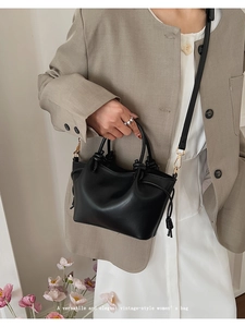 Detail of a black leather bucket bag with drawstring and knot accents on a model
