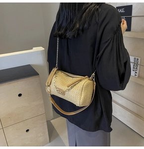 Detail of cylindrical straw shoulder bag with brown leather strap and golden chain link