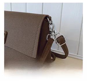 Detail of silver metal hook and textured brown synthetic leather strap on shoulder bag