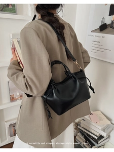 Detail of black tote bag with knot decor and shoulder strap worn over a brown blazer