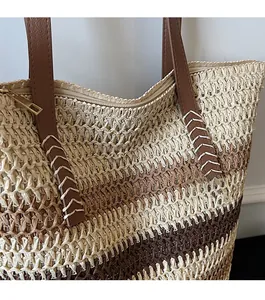 Detail showing reinforced leather strap with stitching on a striped woven straw tote bag
