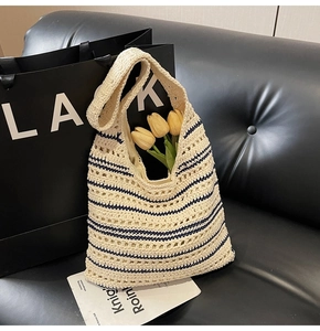 Detail of hollow woven straw tote bag with navy blue stripes on a black leather sofa