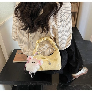 Détail du sac plissé jaune avec pendentif cœur et breloque ours en peluche sur un banc