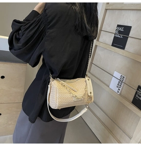 Detail of beige straw cylinder bag with white leather strap and gold chain shown on shoulder
