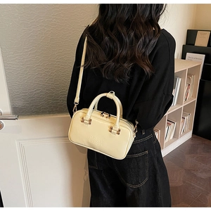 Detail view of the cream leather handbag showing the embossed logo and gold-tone zippers