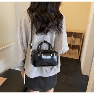 Rear view of model wearing a black glossy leather handbag with gold metal hardware