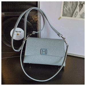 Close-up of blue knit texture flap bag featuring a metal M logo on a stylish table