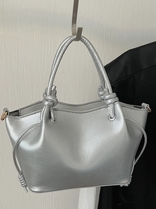 Minimalist silver metallic handbag with unique knot handles and sleek polished texture