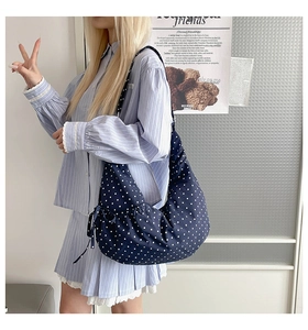 Detail of navy blue polka dot canvas croissant bag with side bow strap on model