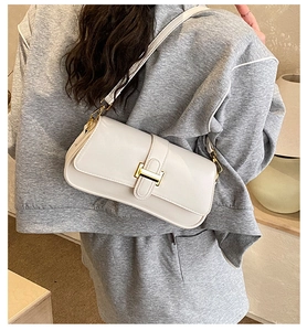 Detail view of cream white shoulder bag with golden metallic clasp on model's back