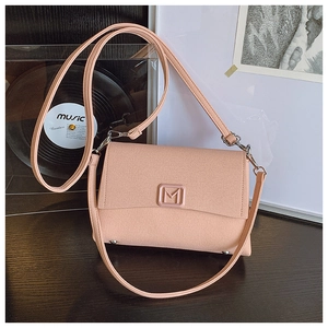 Detailed close-up of a pinkish-orange shoulder bag with a square metal M logo on wood