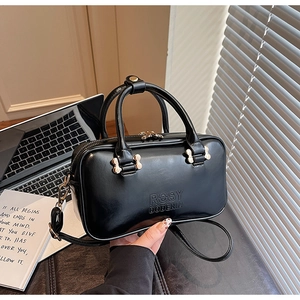 Detail of glossy black handbag featuring embossed logo and premium gold-tone hardware finish