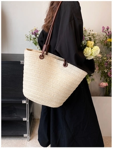 Detail of a large beige straw woven tote bag with brown leather straps worn by a model