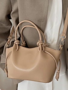 Minimalist beige dumpling handbag with knot details and detachable shoulder strap worn by model