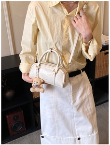 Detail of glossy beige Boston bag featuring a plush bear pendant and chic metal zipper