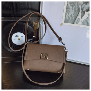 Detail of a brown crossbody bag with cross-grain texture and gold M buckle on vintage desk