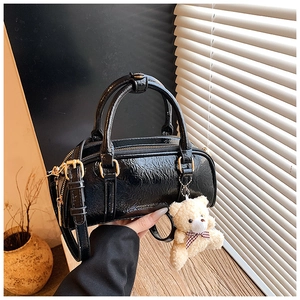 Detail of glossy black Boston bag with ruched texture and a cute plush bear charm