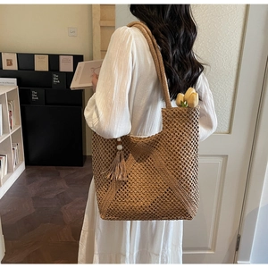 Detail of hand-woven straw tote bag showing diamond openwork mesh and fringe tassel decoration