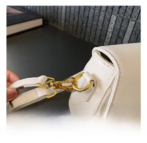 Detail view of the high-quality gold metal hook and white leather strap on a shoulder bag