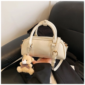 Detail of creamy white textured Boston bag with plush bear charm and leather strap