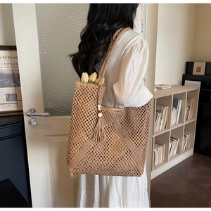 Close-up of woven straw tote bag with crochet hollow pattern and wooden bead tassel