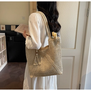 Detail of hollow-out beige woven tote bag with fringe charm on model in cozy interior