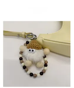 Detail eines weißen Plüsch-Anhängers mit Häkelmütze und Perlenring an einer Ledertasche