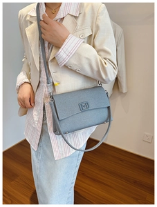 Close-up of a grey textured leather handbag featuring a metal M logo on the front flap