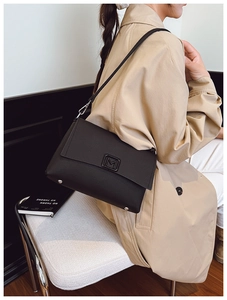 Close-up of black leather bag with M-shaped metal buckle on a trench coat model