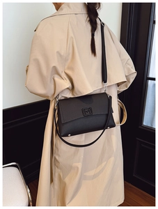 French style black rectangular shoulder bag with metal M buckle shown on a trench coat