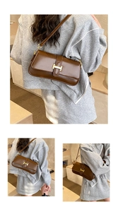 Close-up of brown leather underarm bag featuring a metallic gold H-shaped clasp buckle