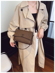 Detail of a brown leather shoulder bag featuring a silver M-shaped metal buckle and strap