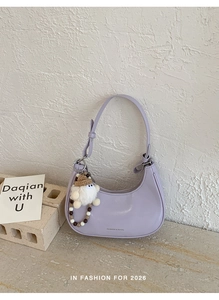 Detail der fliederfarbenen Halbmond-Tasche mit Bärenanhänger und Perlenkette auf Stein