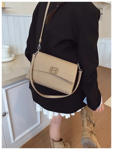 Detail view of gold textured crossbody bag with metal M buckle on model's shoulder