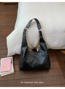 Detail der schwarzen Hobo-Tasche aus Leder mit silbernen Nieten auf Holzboden