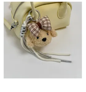 Close-up of a plush puppy charm with a red plaid bow on a yellow handbag strap