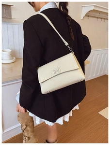 Detail of beige textured fabric shoulder bag with metallic M logo and protective metal studs