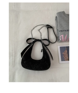 Detail of black quilted crescent bag with bow decoration and metal chain strap