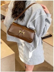 Detail of a brown baguette bag with a gold H-shaped metal buckle on a shoulder strap