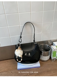 Detail der schwarzen glänzenden Halbmond-Hobo-Tasche mit Logo und Plüsch-Anhänger