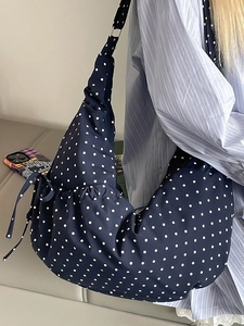 Navy blue polka dot canvas crescent bag with side drawstring shown on shoulder