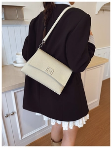 Detail of creamy white leather crossbody bag with a metal M-shaped buckle and fine texture