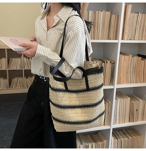 Close-up of a woven straw tote bag with black stripes and elegant faux leather straps
