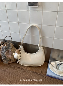 Nahaufnahme der cremefarbenen Hobo-Tasche mit Zwergenanhänger auf Holzgrund