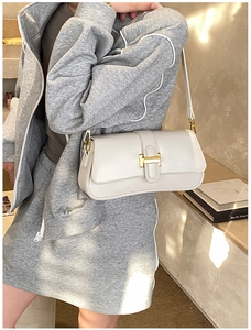 Detailed close-up of a minimalist cream shoulder bag with a gold H-shaped metal buckle