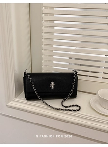 Detail of black lychee grain leather handbag with silver clasp and chain on a windowsill