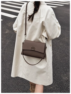Detail of a brown leather crossbody bag featuring a gold M-shaped metal buckle and strap