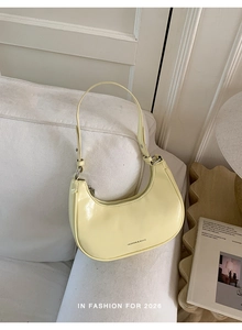 Detailansicht einer hellgelben Halbmond-Tasche mit Silberbeschlägen auf weißem Sofa