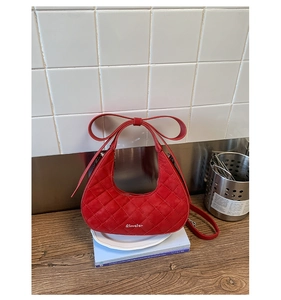 Detailed view of red quilted crescent bag with bow-shaped handle and silver metal logo