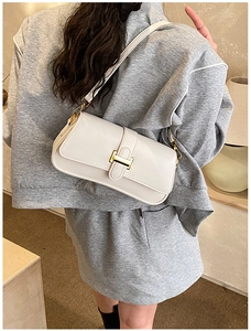 Detail of a creamy white glossy leather shoulder bag featuring a gold H-shaped metal buckle